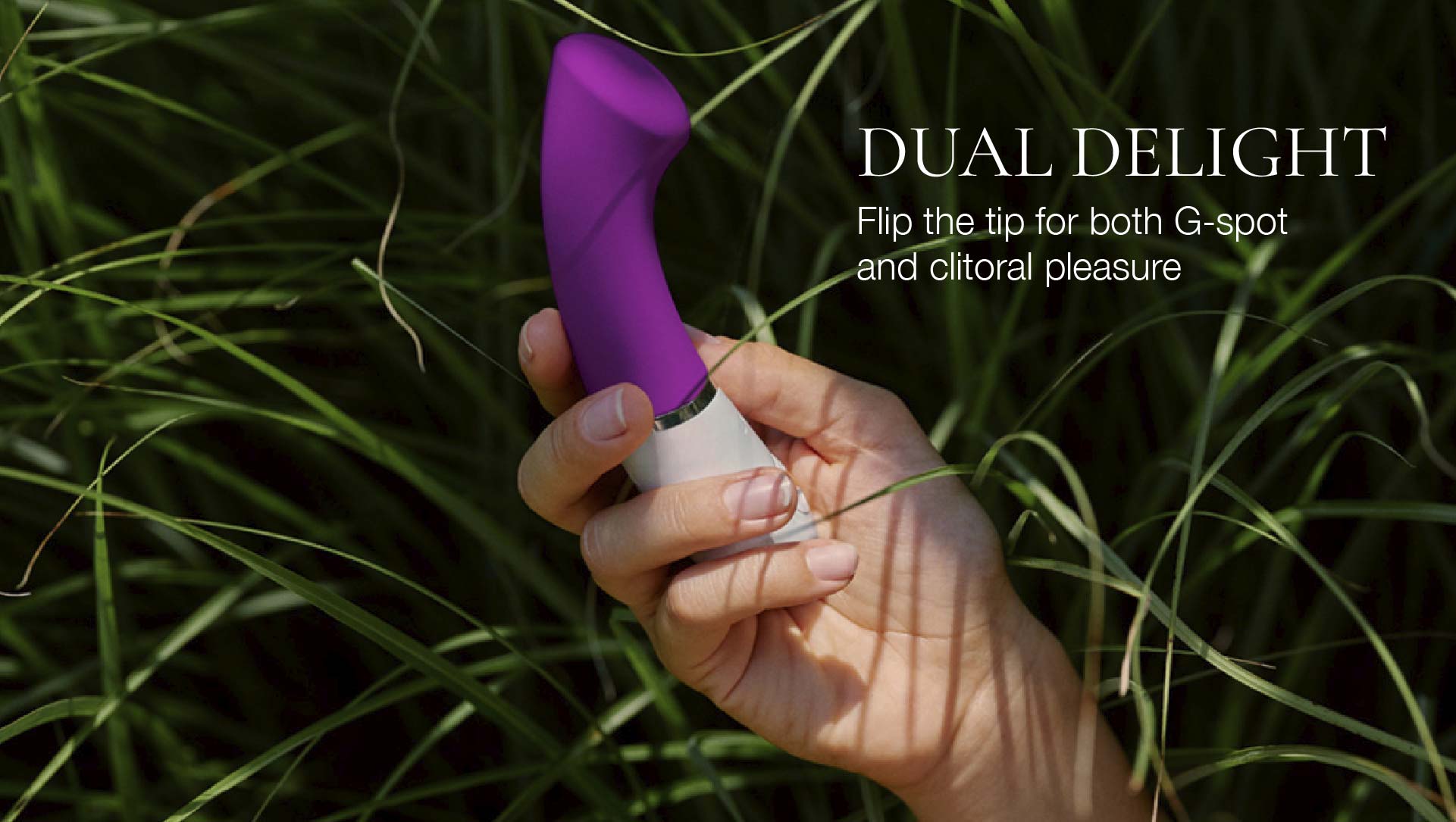 Hand holding a purple and white dual-purpose vibrator against a grassy background