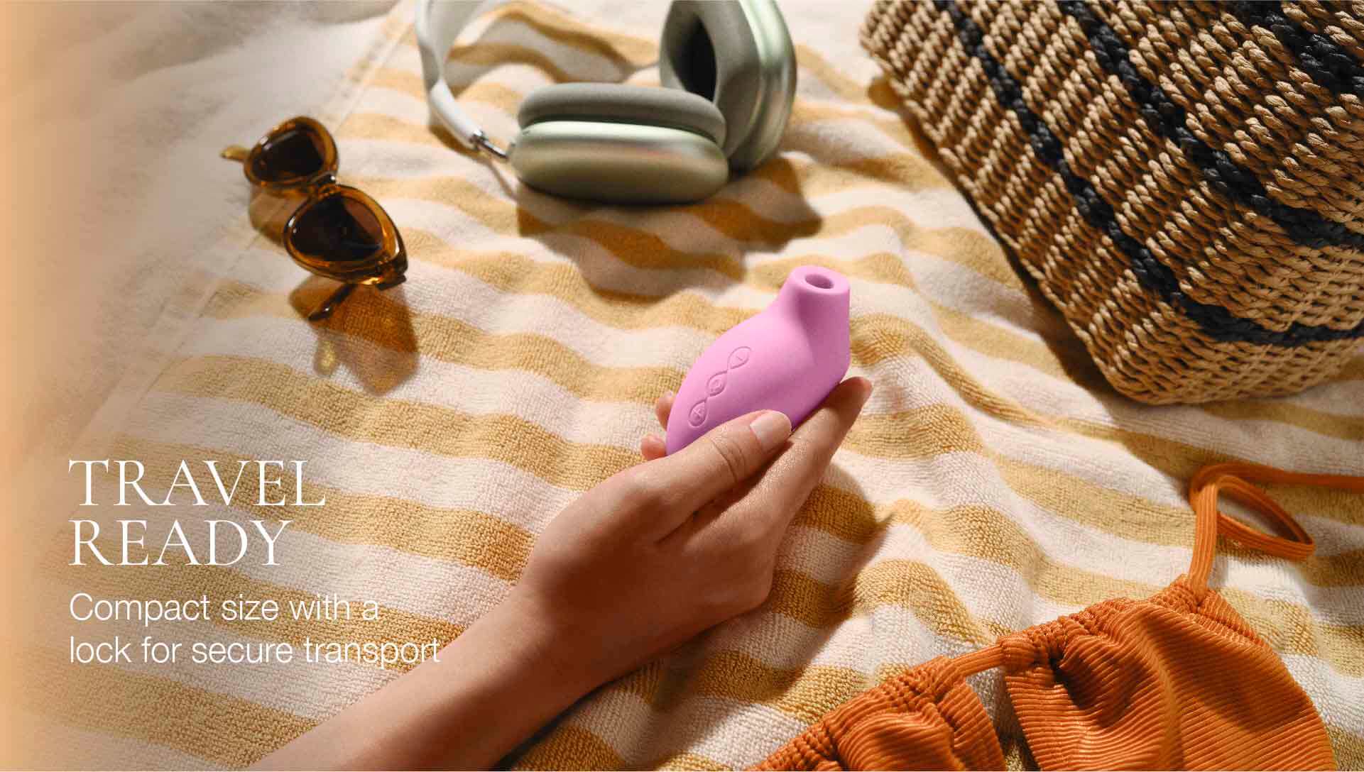 Hand holding a pink travel vibrator on a striped fabric background with sunglasses and a basket.
