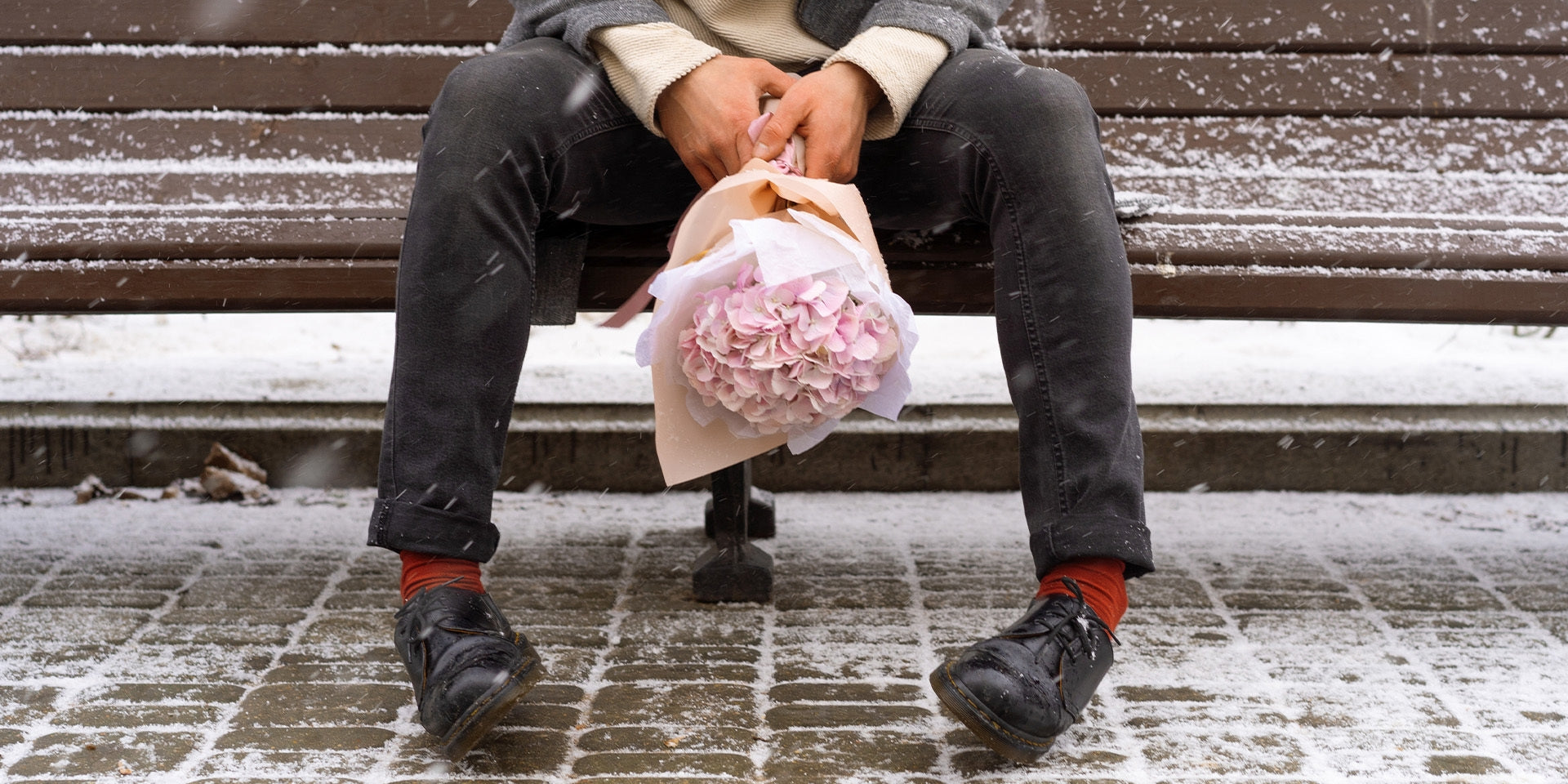 Man sitting on a bench in the snow holding a bouquet of roses