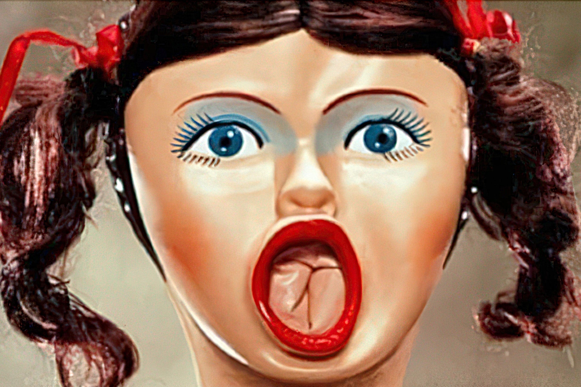 Close-up of a campy novelty inflatable doll face with exaggerated eyes, pigtails, and open mouth.