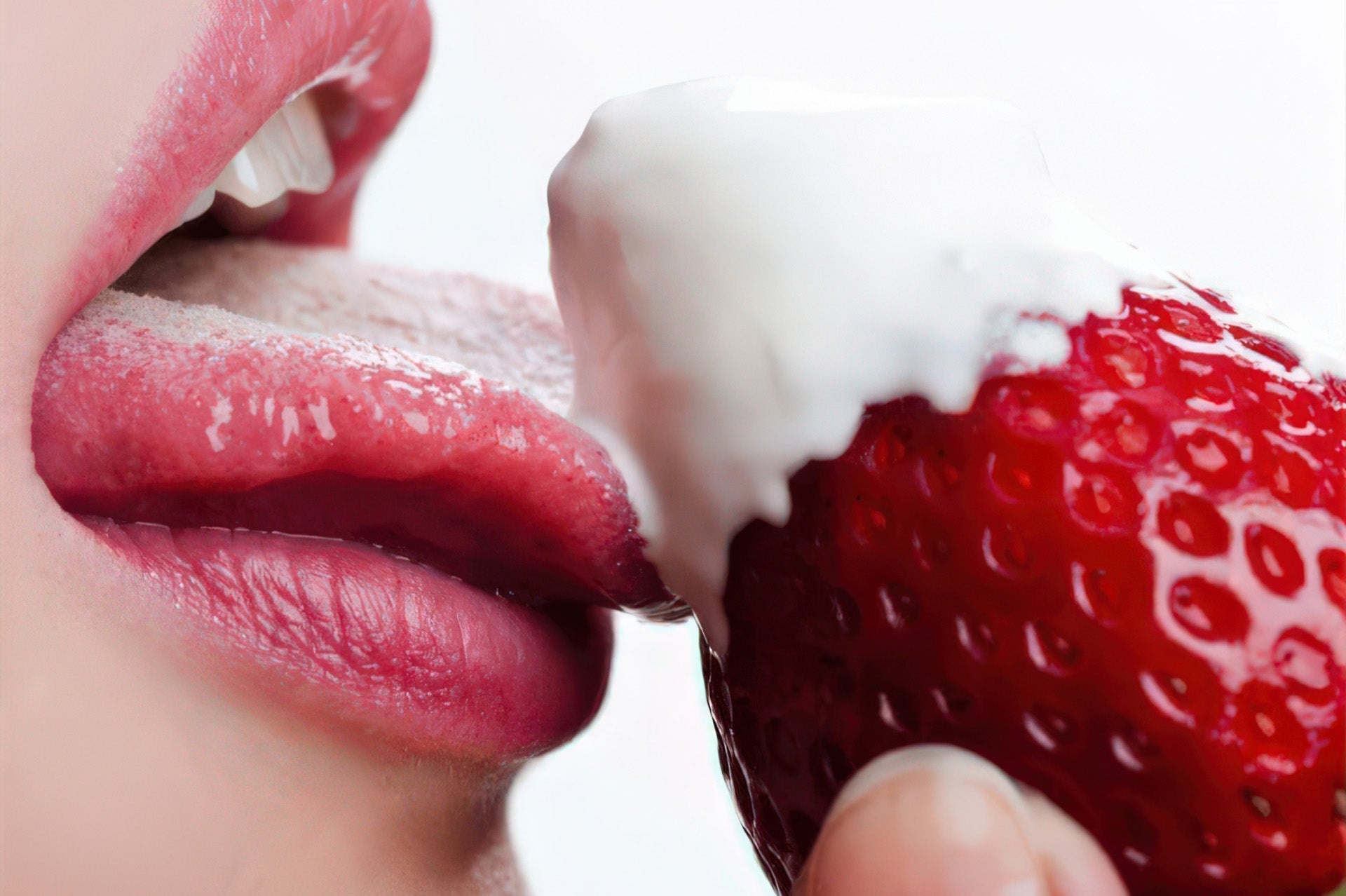Close-up of parted lips with a tongue licking a cream-topped strawberry against a white background.