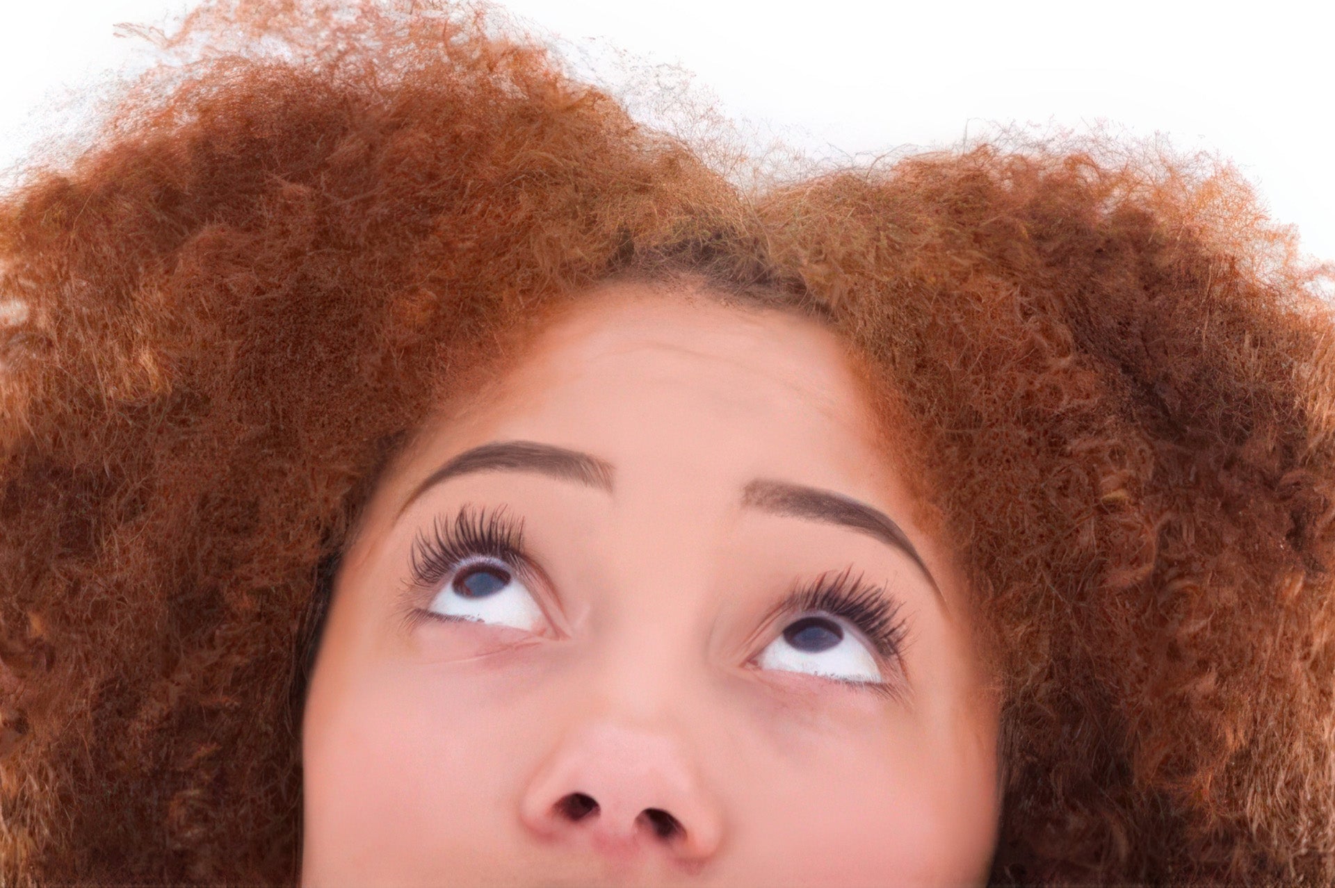 Tight crop of a woman's face from nose up, looking upward with wide curious eyes and full natural hair.