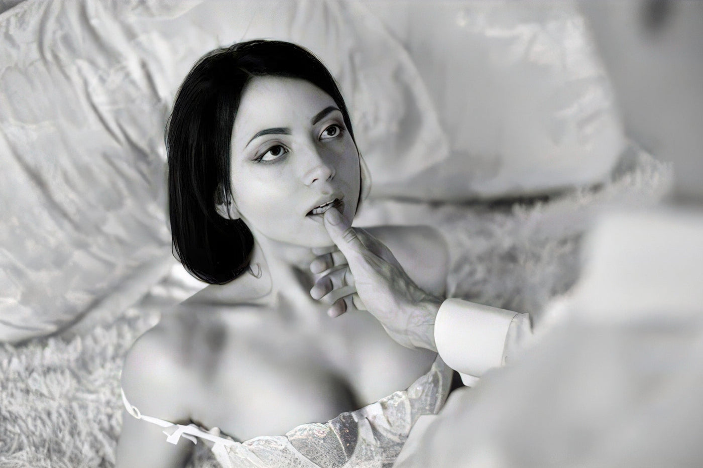 Black-and-white photo of a dark-haired woman in a corset looking up as a man's hand touches her chin.