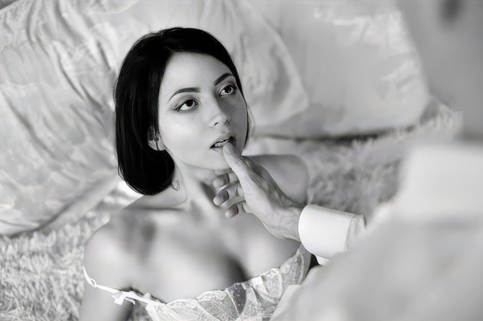 Black-and-white photo of a dark-haired woman in a corset looking up as a man's hand touches her chin.