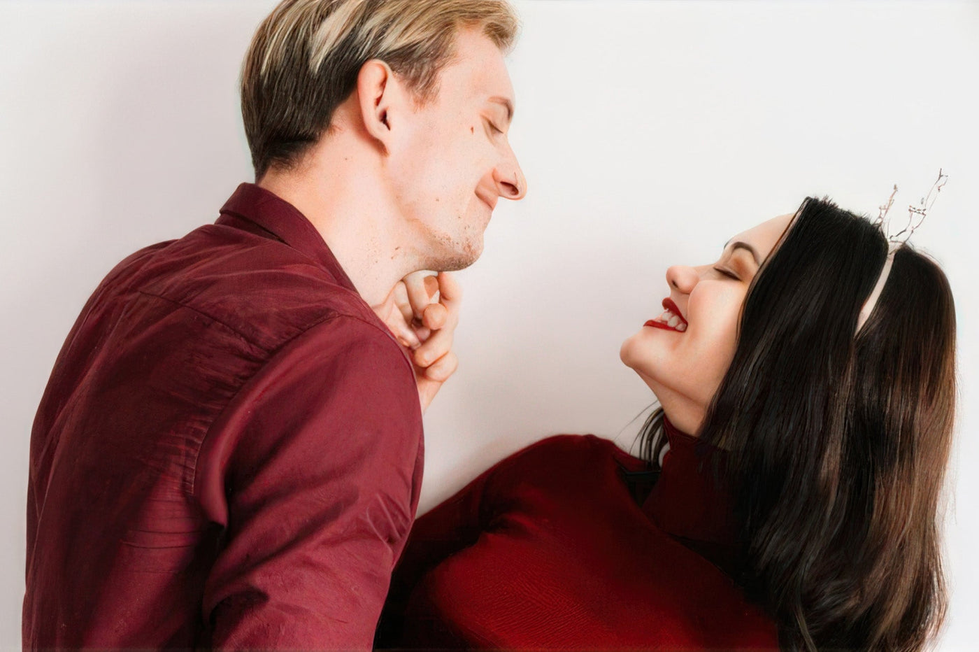 A couple in red and burgundy leans close, smiling face-to-face against a white background with Valentine's décor.