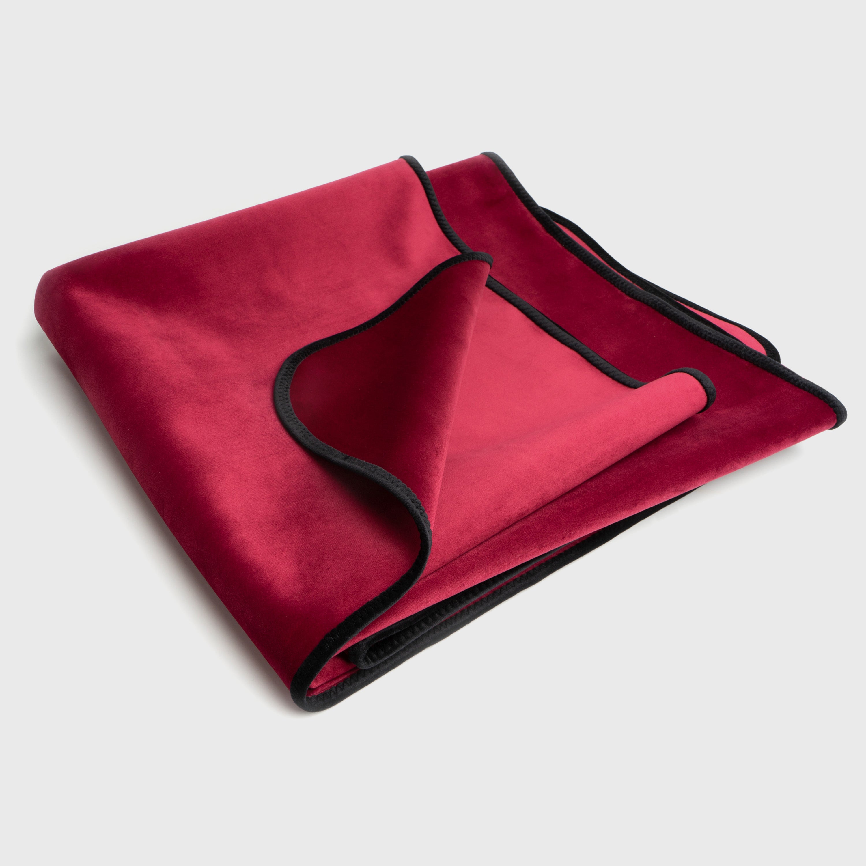 Folded red blanket with black trim on a light gray background