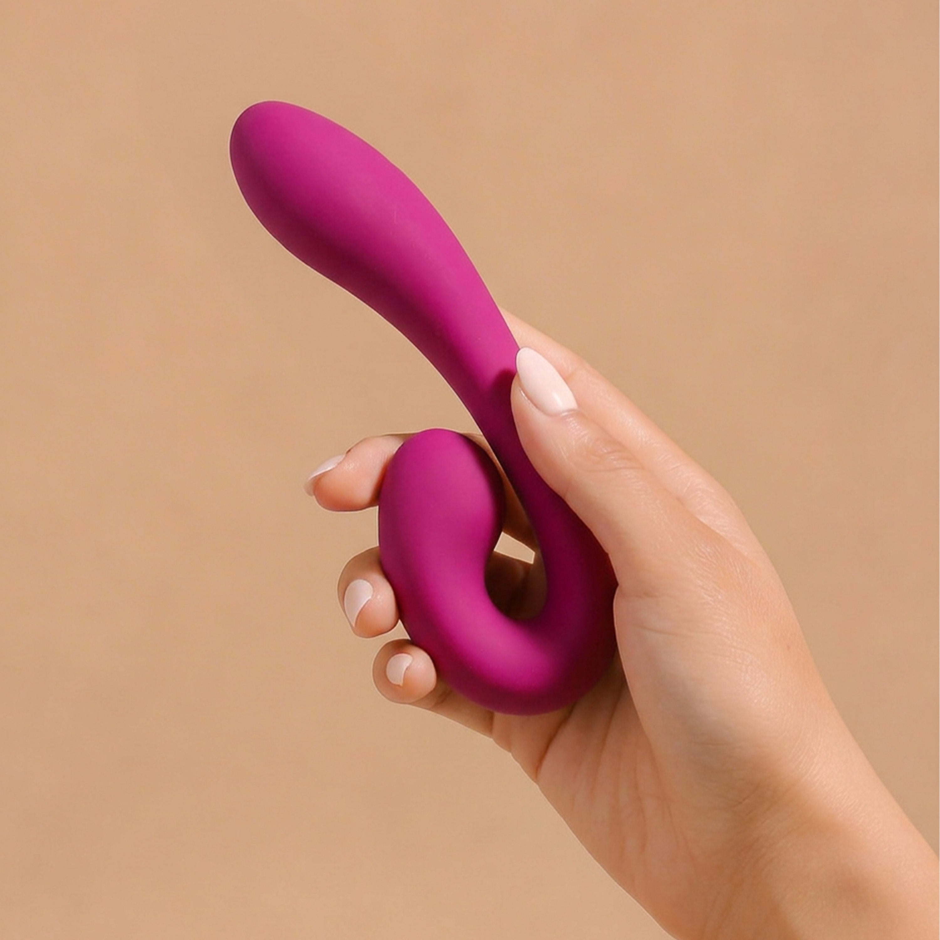 Hand holding a pink silicone vibrator against a beige background