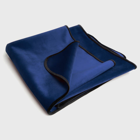 Folded blue blanket with black trim on a light gray background