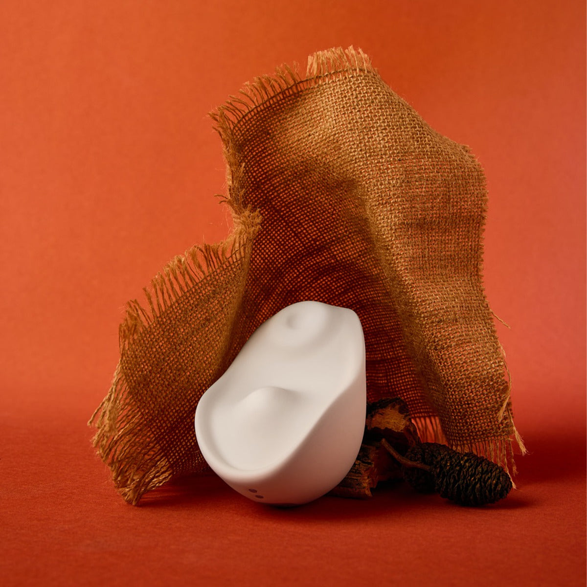 White version of the Kiss vulva tapping and heated vibrator by Osuga on an abstract burlap display