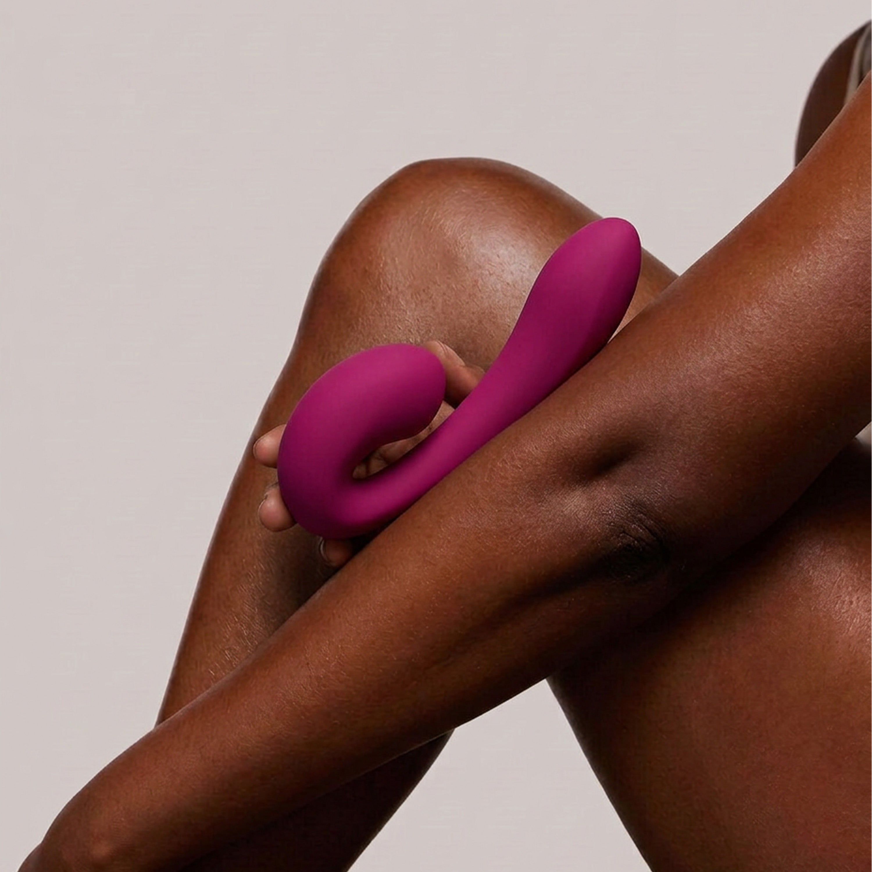 Person holding a pink massager against their leg on a beige background