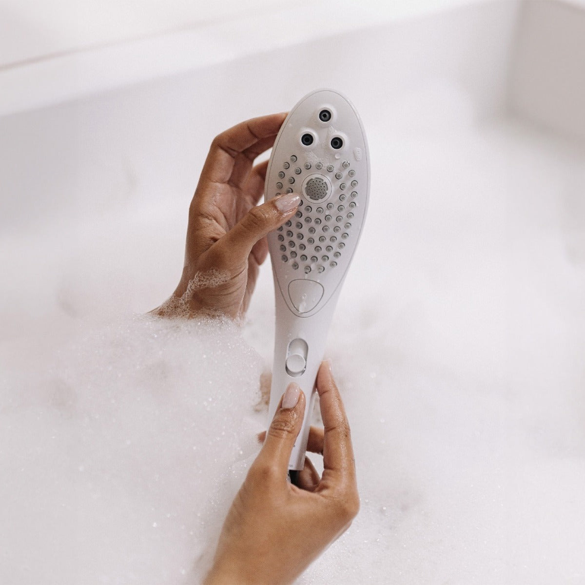 Hand holding a white showerhead with a bathtub in the background