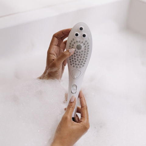 Hand holding a white showerhead with a bathtub in the background