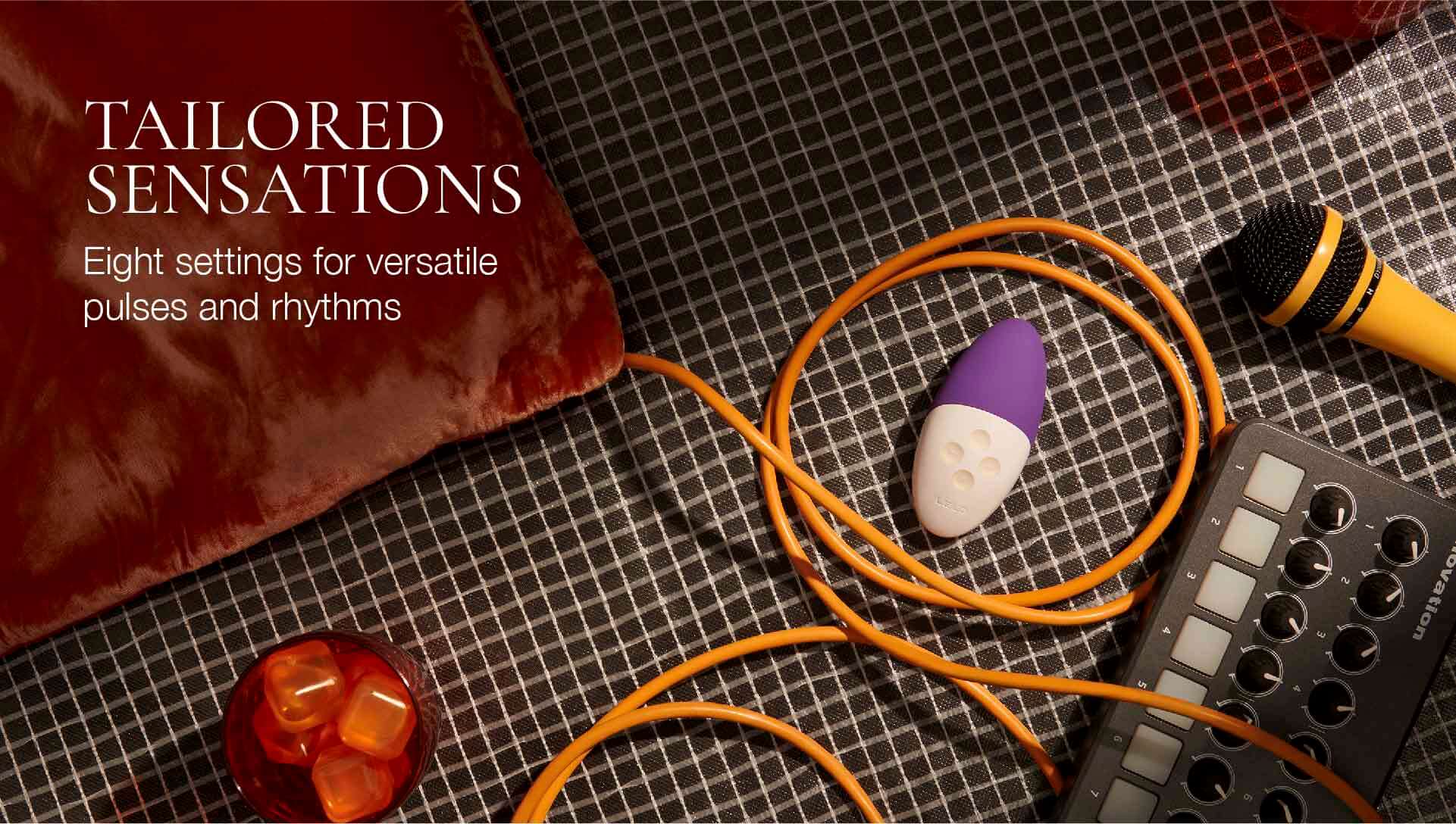 Orange cable, purple and white stone, red object, and electronic device on a textured surface with text 'Tailored Sensations'.