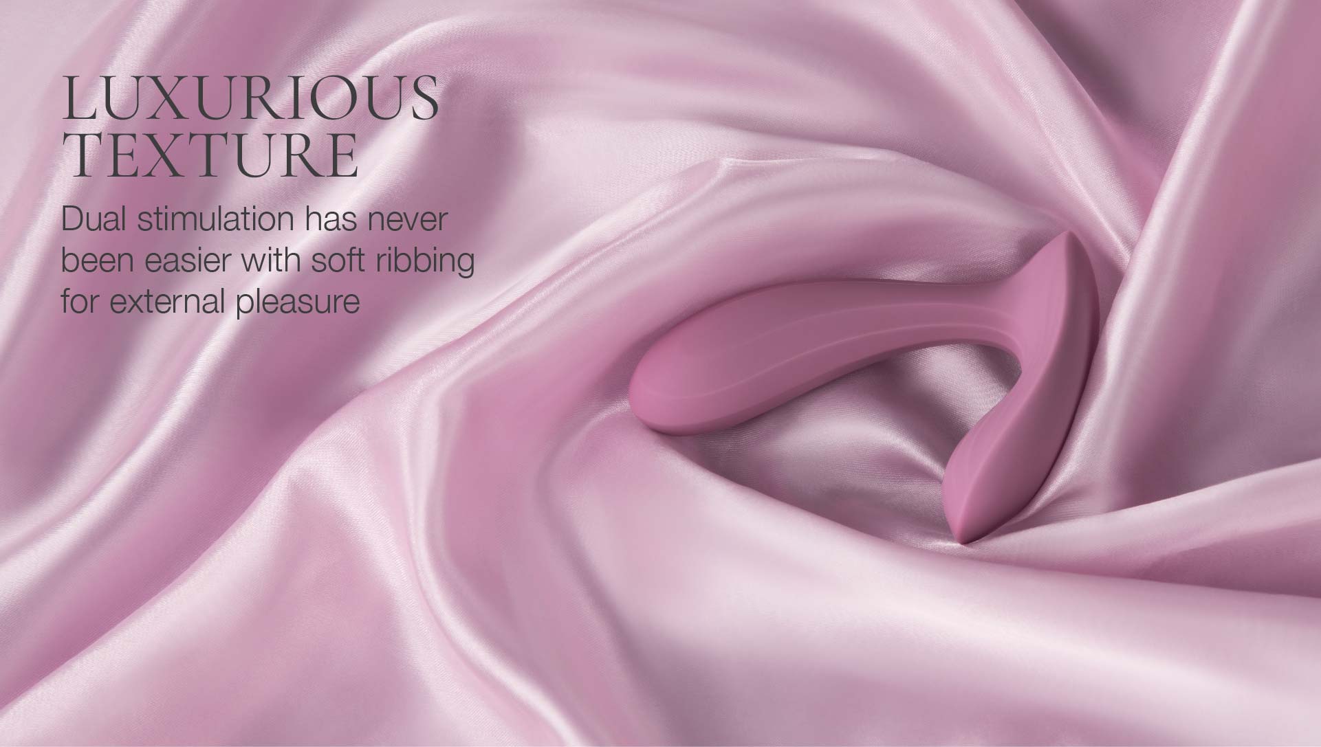 Pink silicone vibrator on pink satin fabric with text about luxurious texture and dual stimulation.