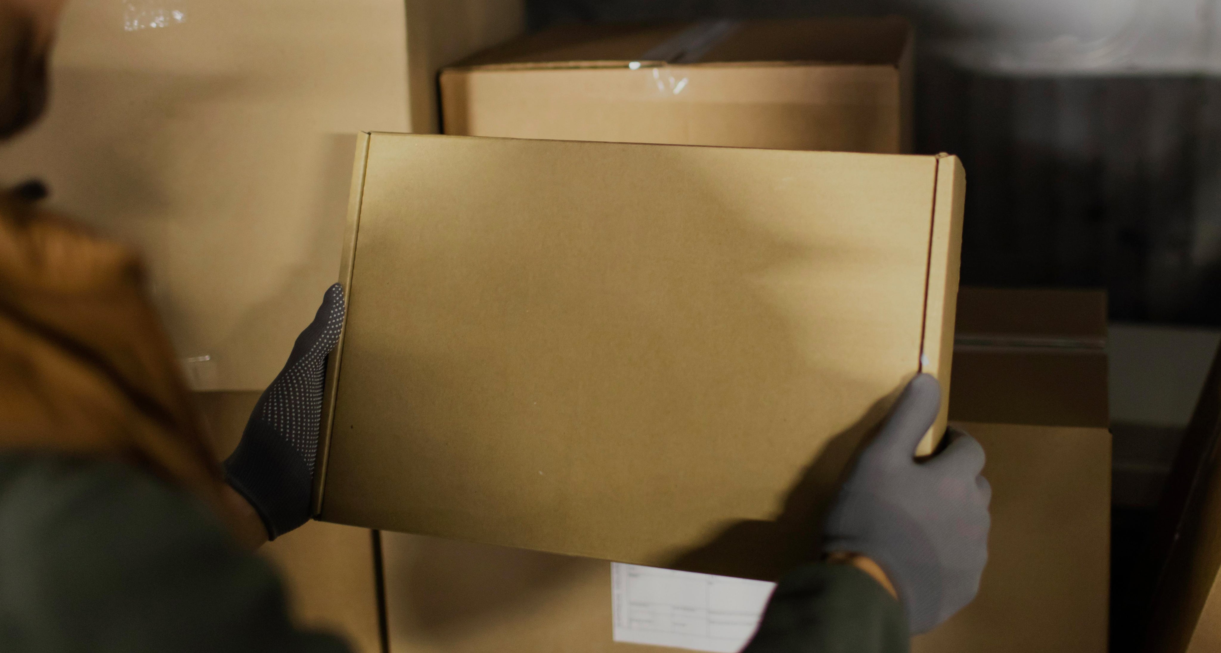 Person wearing gloves holding a cardboard box in a dimly lit room.