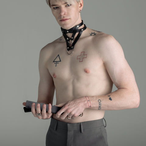 Man with tattoos holding a leather slapper against a gray background