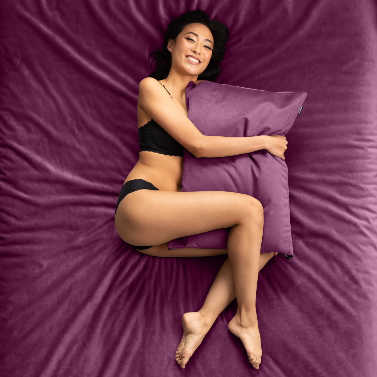 Woman lying on bed cuddling with a Fascinator Pillowcase between her arms and legs
