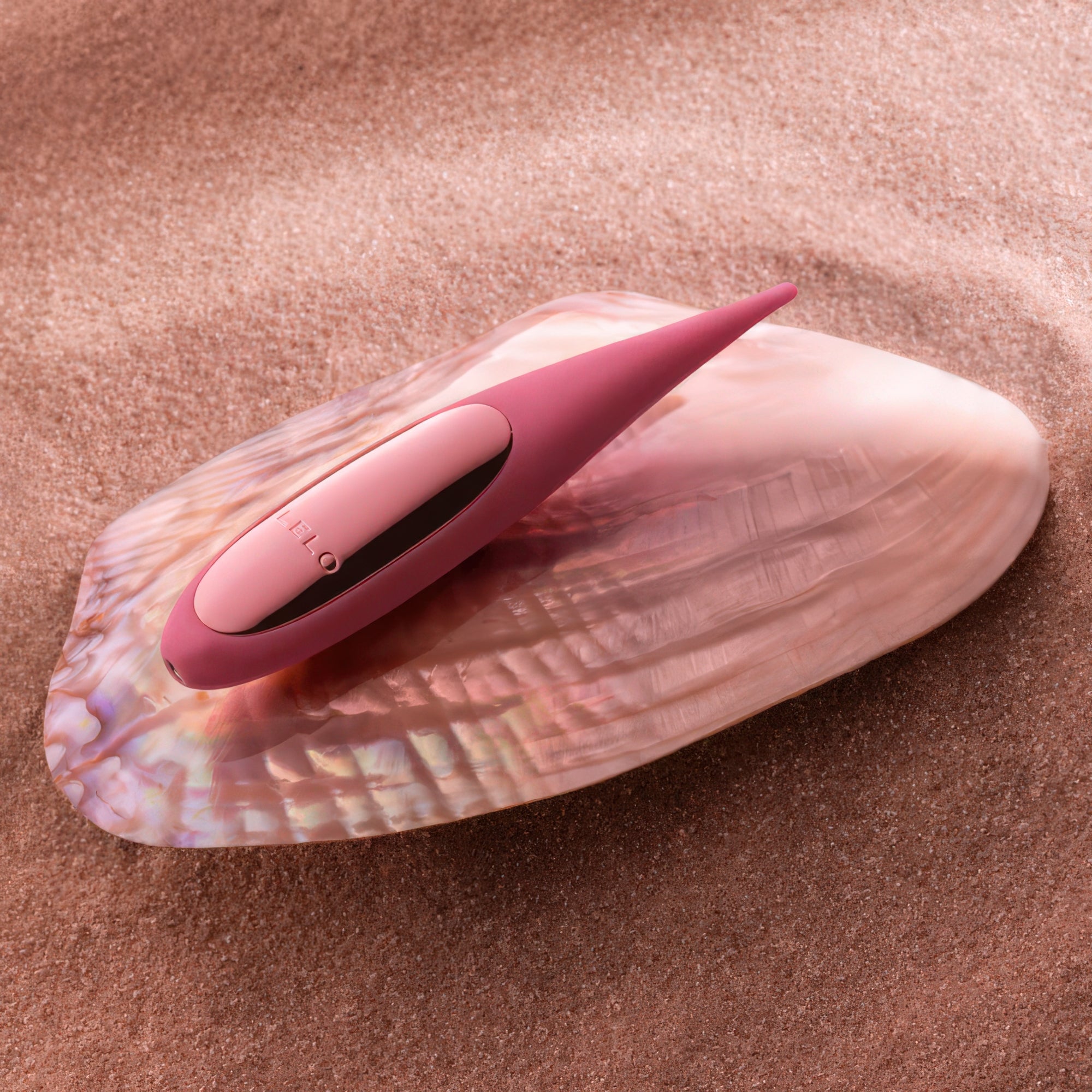 Pink electronic device on a seashell with sand background