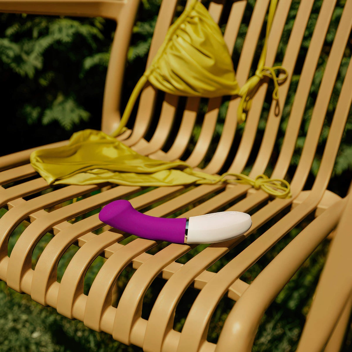 LELO Gigi 3 in Purple sitting on an outdoor chair with a green bikini top tossed over the back of the chair
