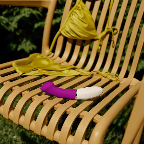 LELO Gigi 3 in Purple sitting on an outdoor chair with a green bikini top tossed over the back of the chair
