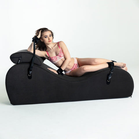 Woman in pink lingerie lying on a black foam chaise against a white background