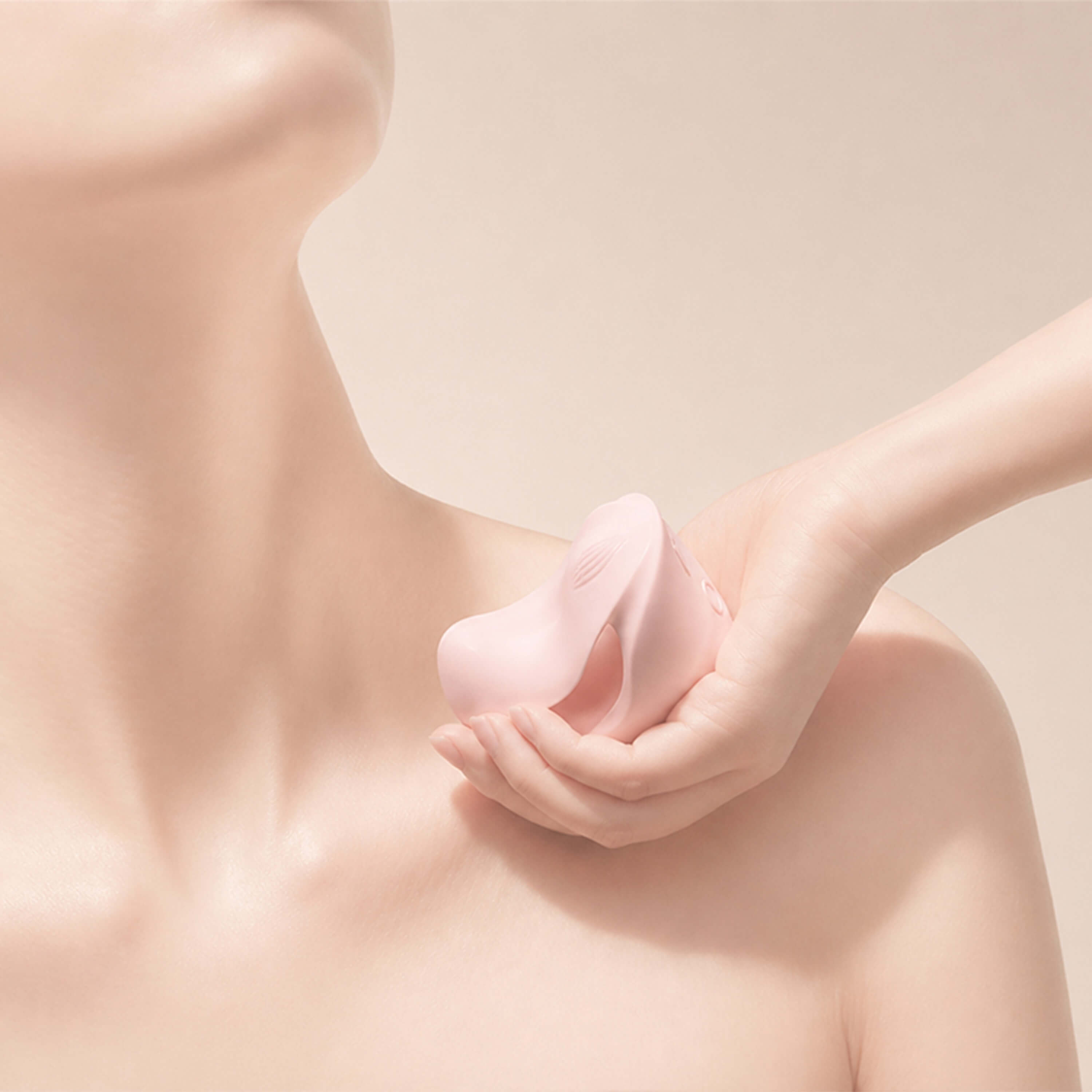 Close-up of a hand holding a silicone vibrator against a beige background