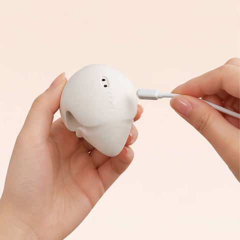 White wireless vibrator being plugged into a charging case held by a hand on a beige background