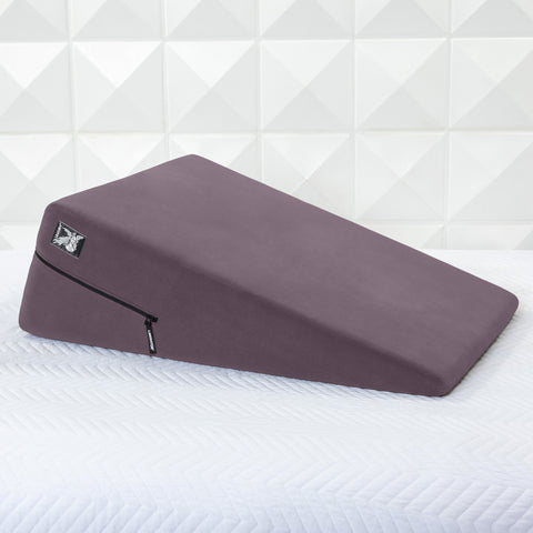Purple wedge pillow on a white mattress with a geometric patterned wall in the background