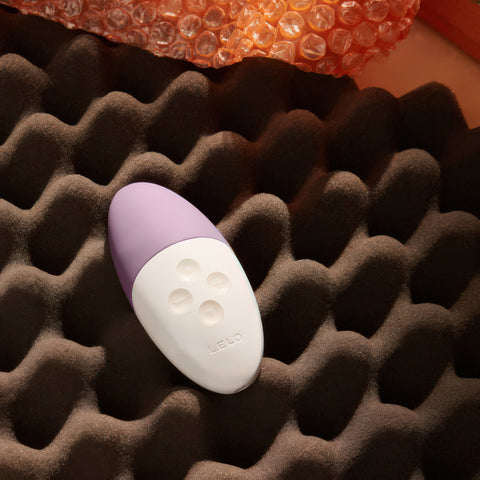 Purple and white vibrator on a textured brown surface with an orange object in the background