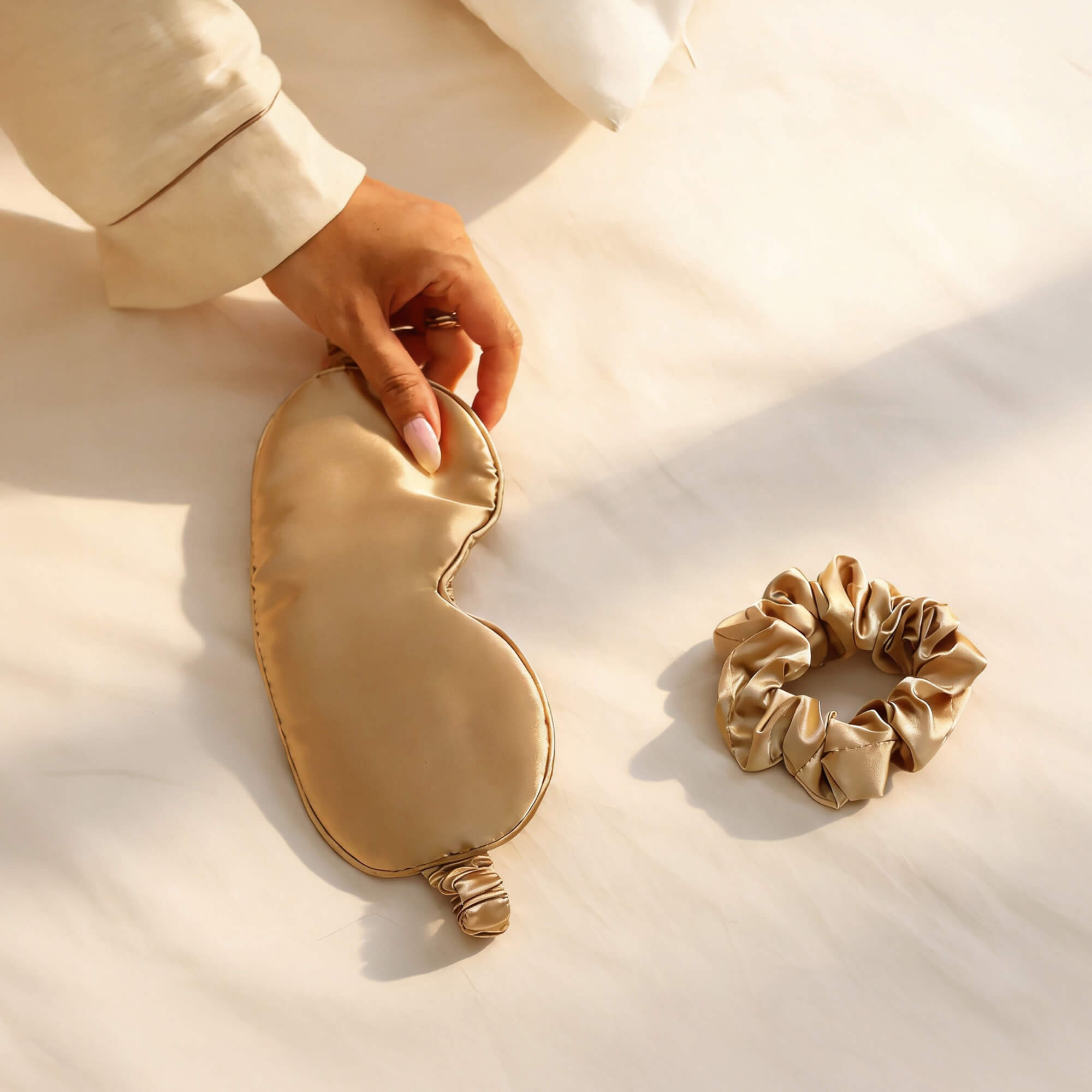 Beige satin eye mask and scrunchie on a light beige surface