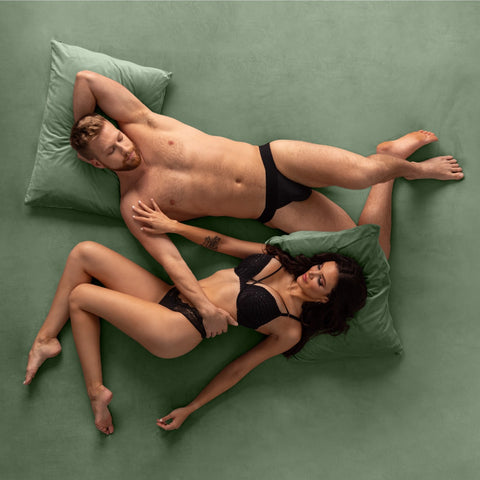 Couple lying on their backs and looking at each other on a sage green Vadot Velvet Sheet Set from Liberator®