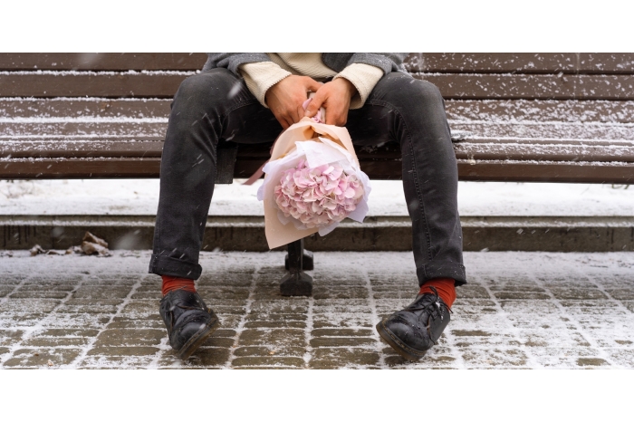 Man sitting on a bench in the snow holding a bouquet of roses